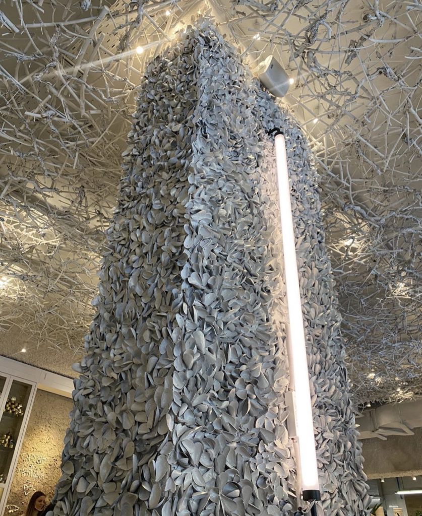 Tall decorative column wrapped in sculptural leaf elements with integrated ceiling installation for Dubai venue